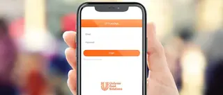 Eine Hand hält ein Smartphone in die Bildmitte. Auf dem Display ist die Lead-App für UFS zu sehen. Im Hintergrund ist verschwommen eine belebte Fußgängerzone zu erkennen.