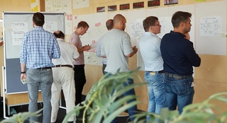 Mehrere Personen stehen bei einem Workshop vor Whiteboards.