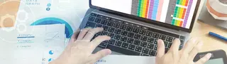 Laptop mittig auf Schreibtisch, daneben liegen Auswertungen und Diagramme.