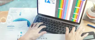 Laptop mittig auf Schreibtisch, daneben liegen Auswertungen und Diagramme.