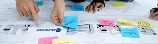 Personen kleben farbige Post-Its auf die Übersicht eine Customer Journey, welche auf einem Tisch liegt.
